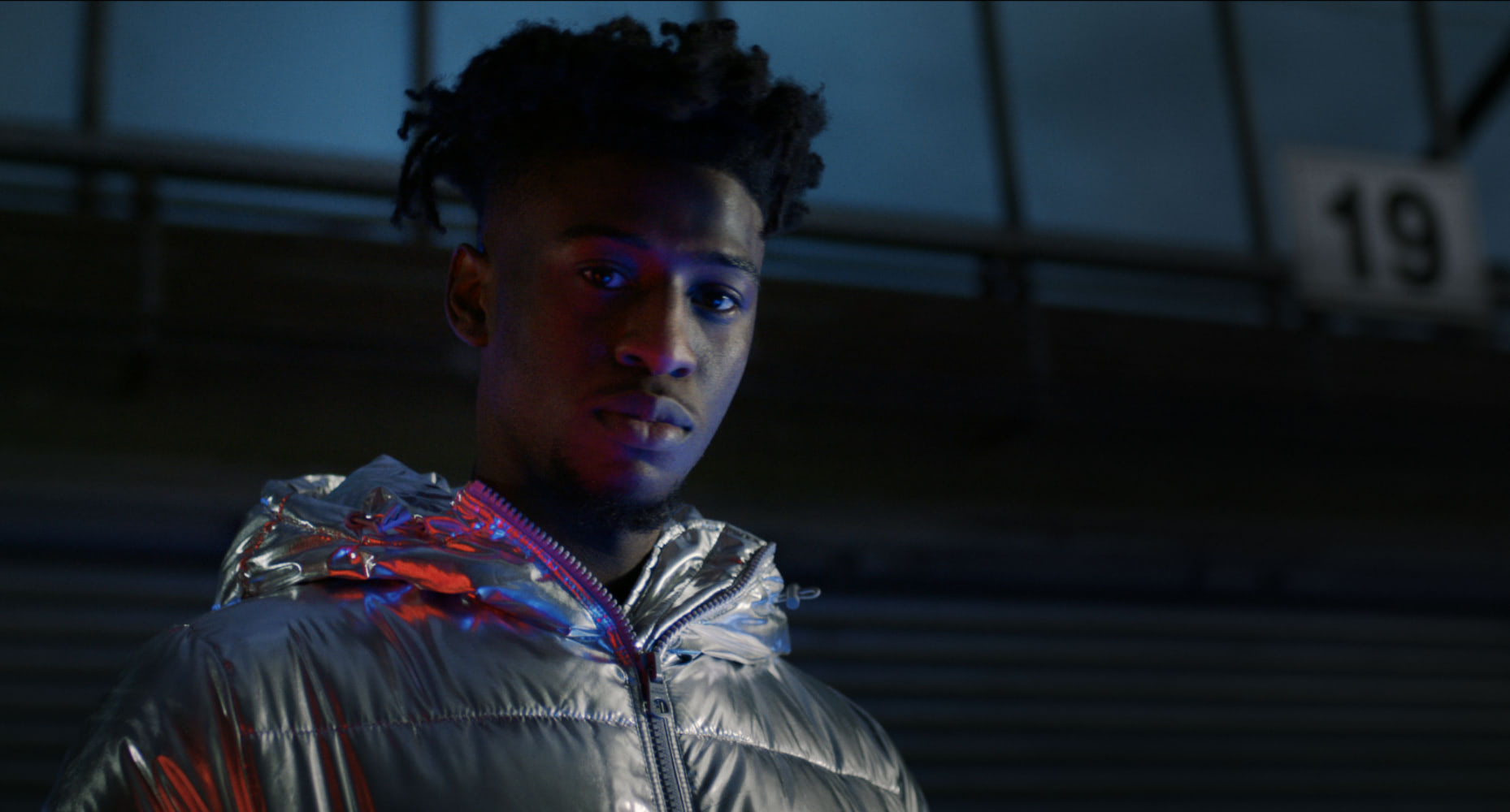 A young man wearing a silver jacket inside a garage.