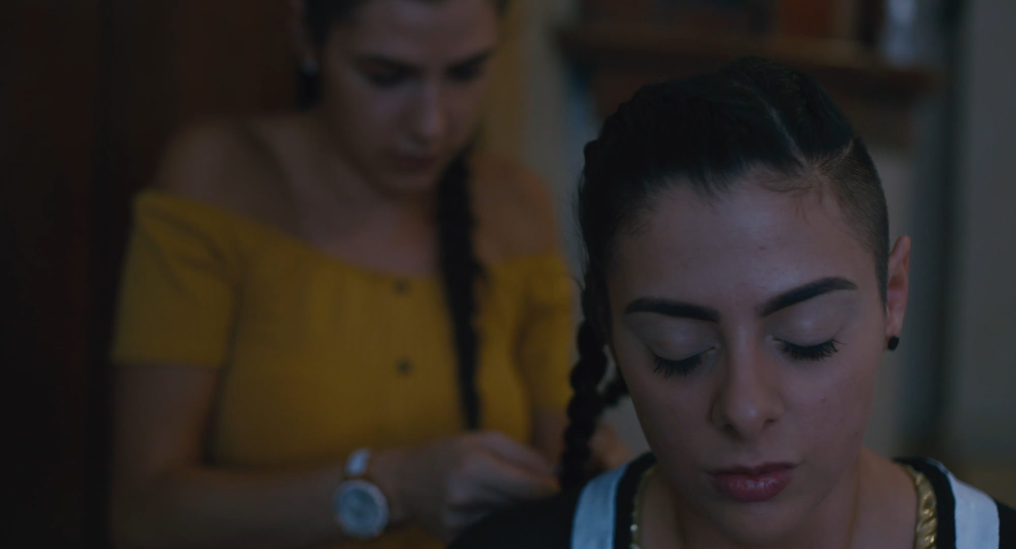 A young woman with her eyes closed has her hair braided by another woman behind her.