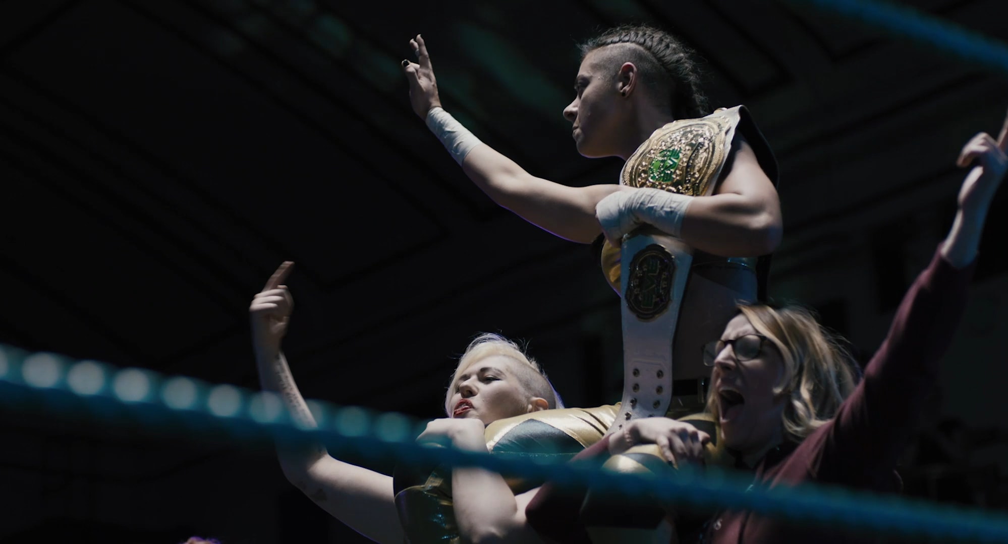 A young woman, trophy in hand, is being carried by two other triumphant women.