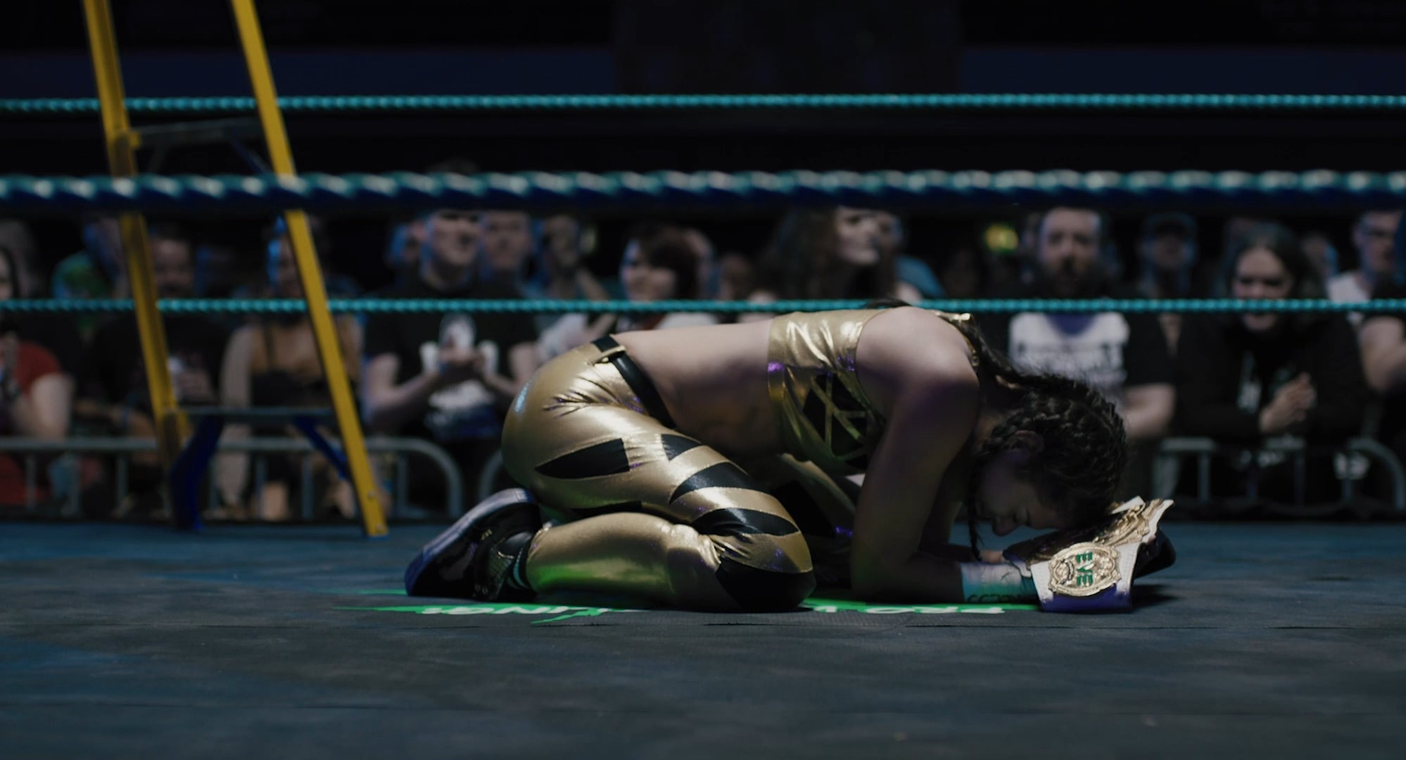A young woman overcome with emotion kneeling in the wrestling ring, embracing a trophy