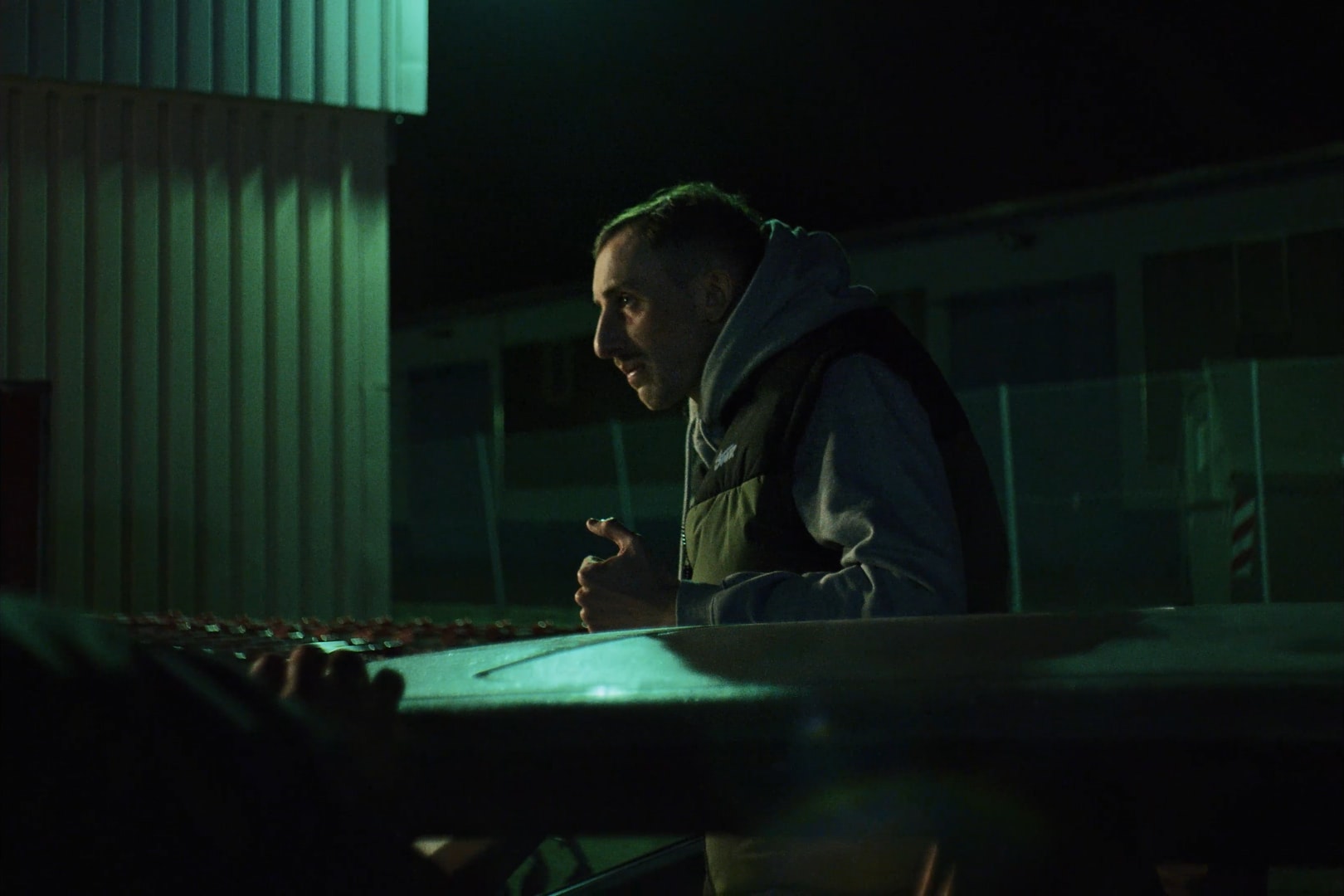 A man standing at night outside his car, looking intently at something outside the frame