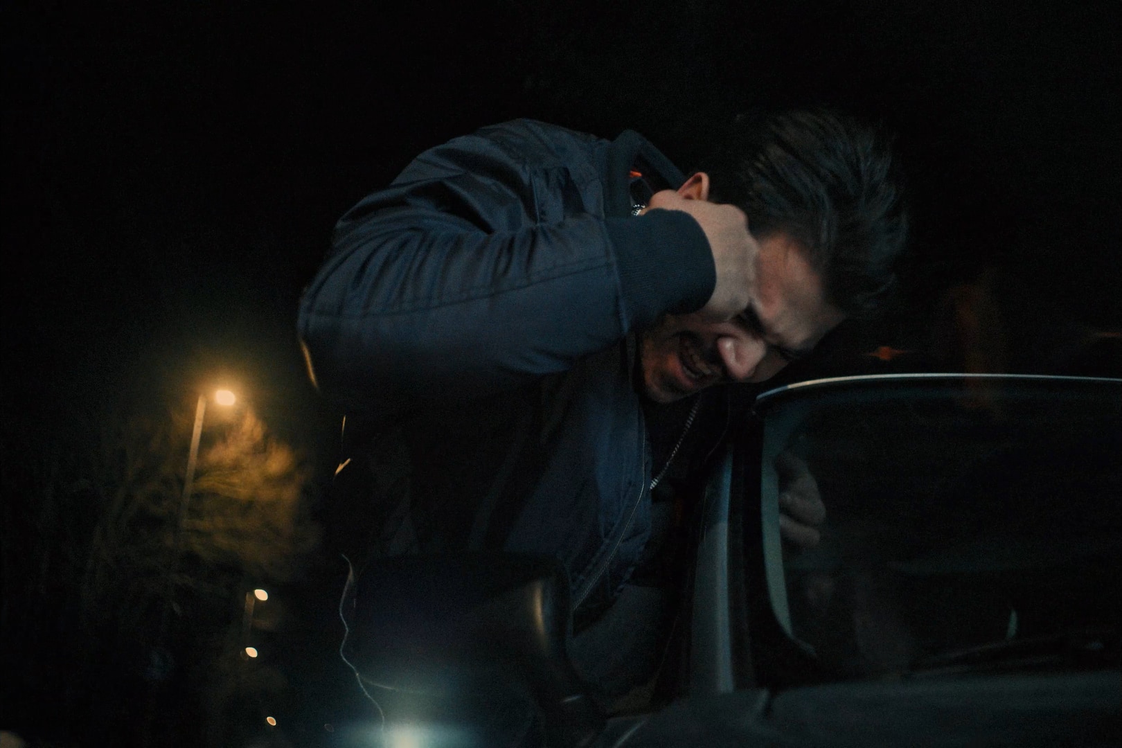 Young man leaning outside the window of a car, punching his head