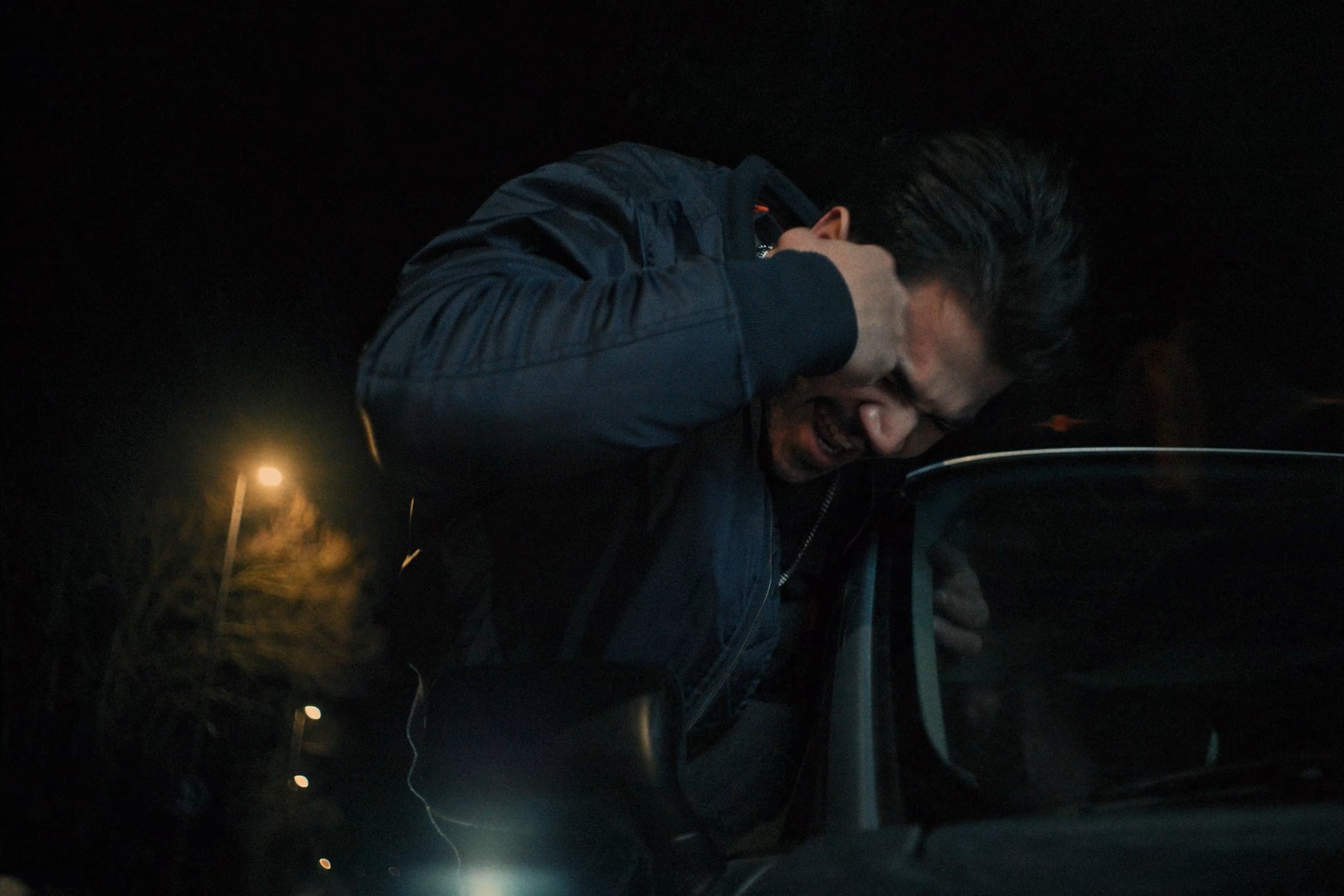 Young man leaning outside the window of a car, punching his head