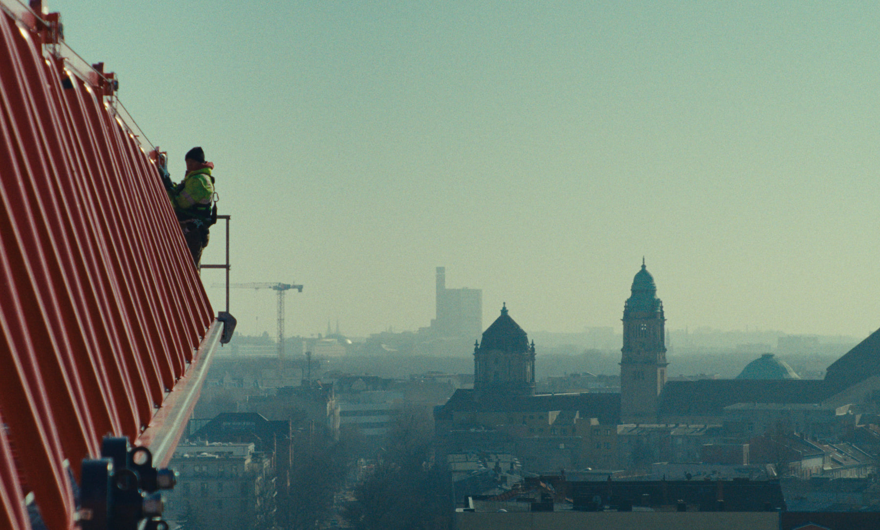 A construction worker standing precarioulsy at the edge of a crane in the sky over Berlin