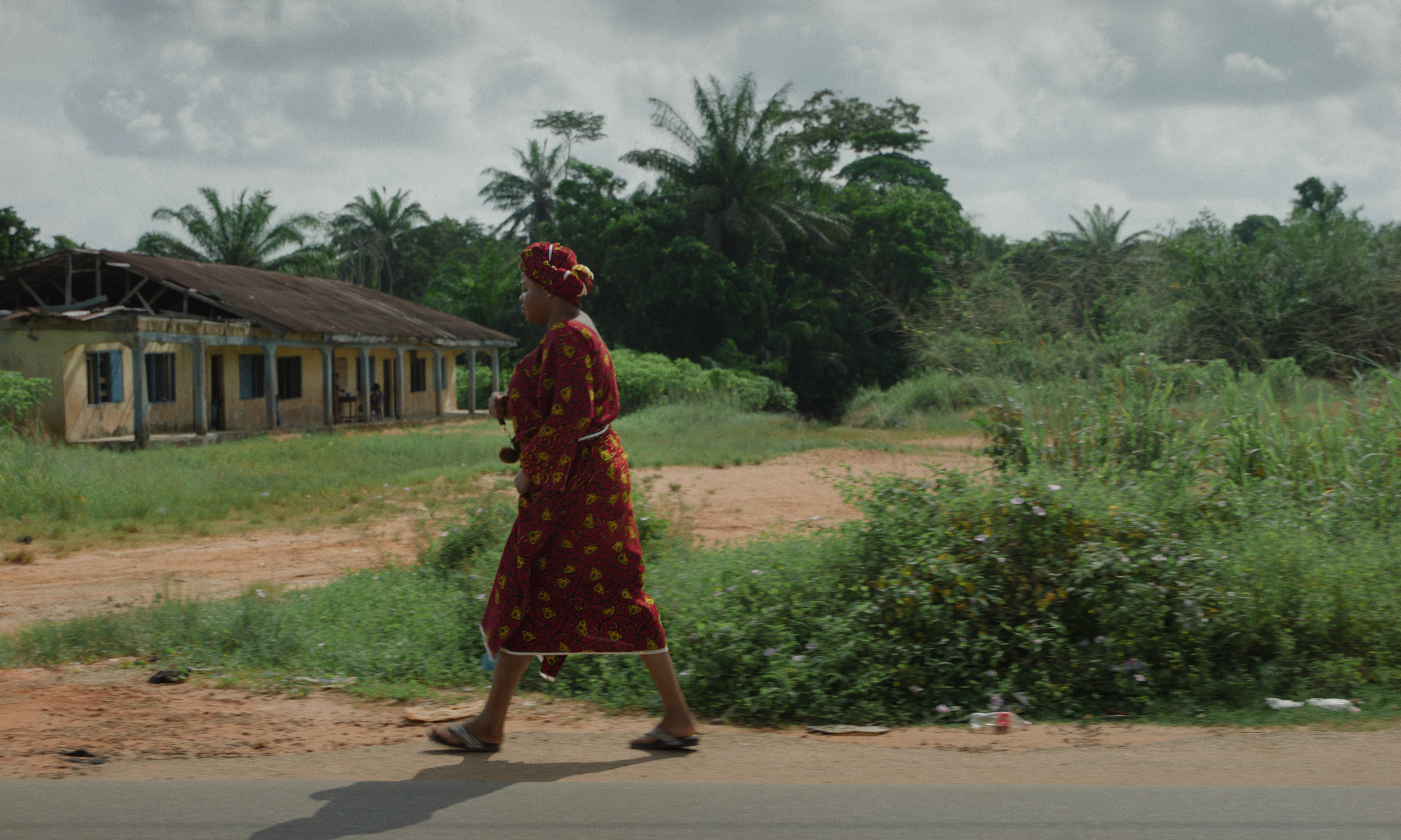 Woman walking along the village road, in the distance a lush green jungle.