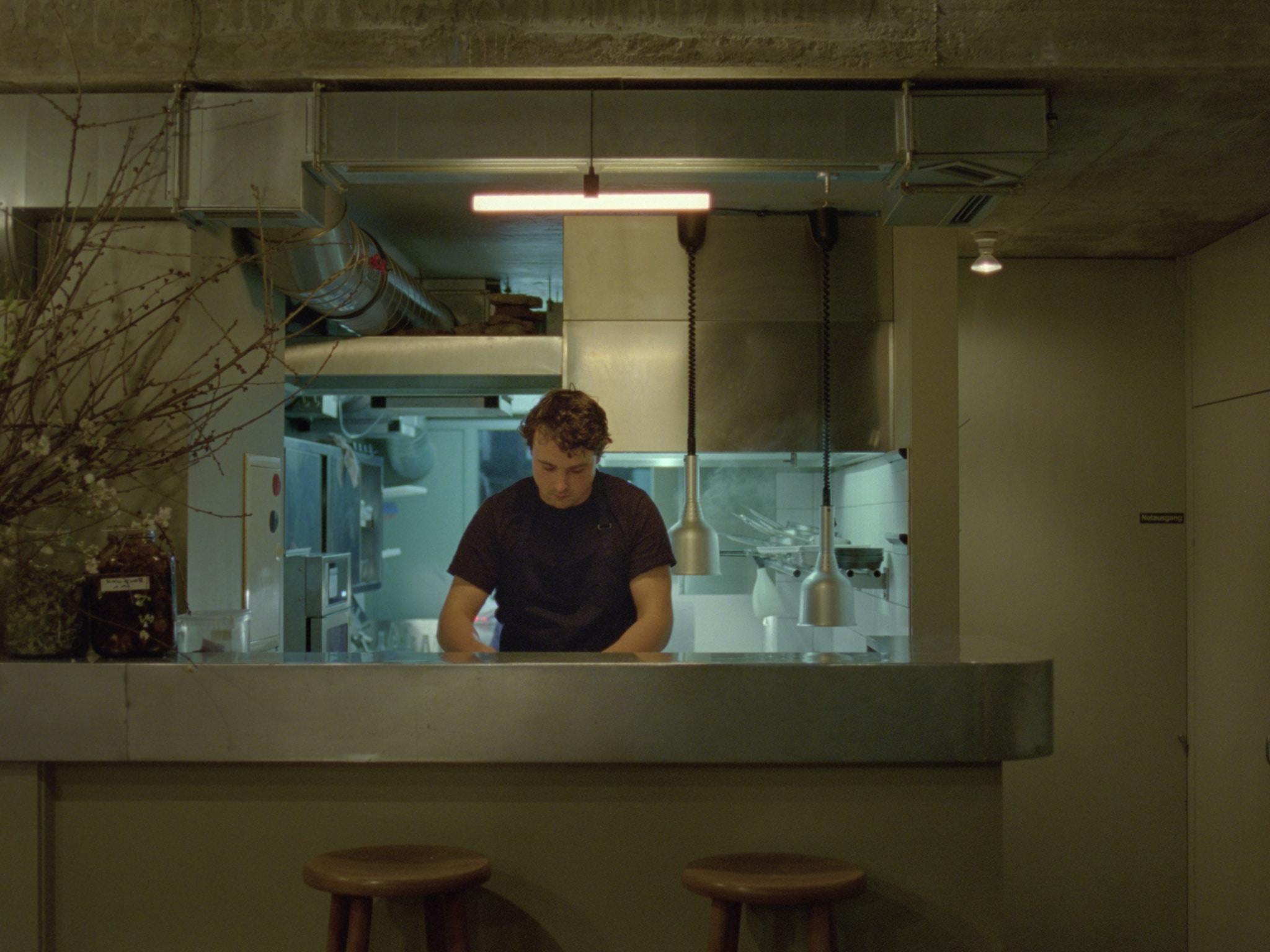 A young chef standing in a restaurant behind a counter, preparing food. 