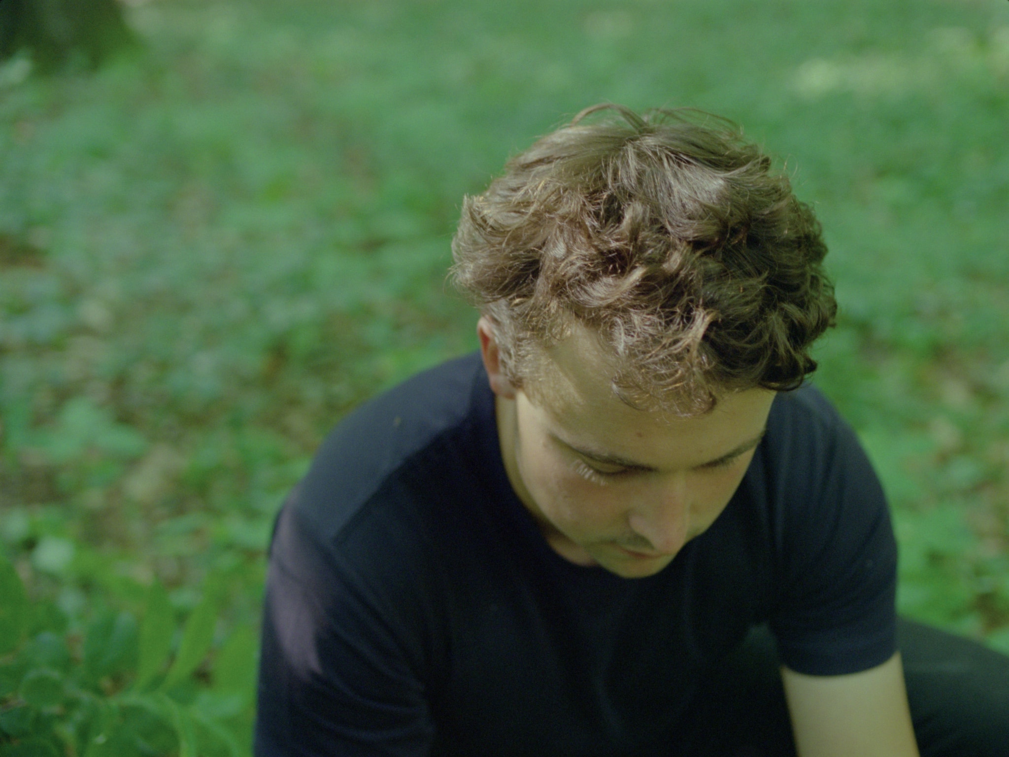 The face of a young man seen from above kneeling on the forest ground.