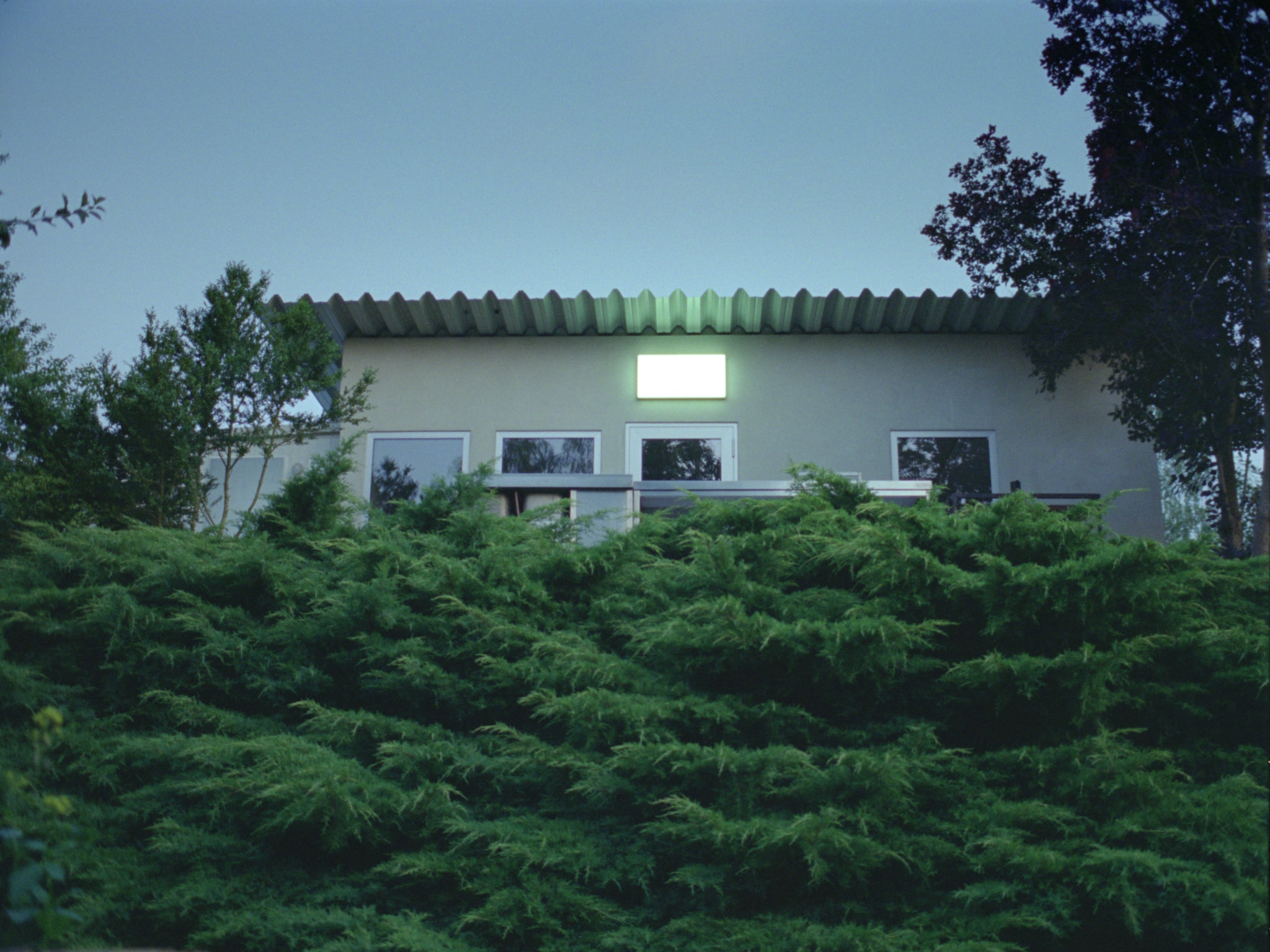 A small cottage at dusk, the light on the porche switched on, seen from the hill below.