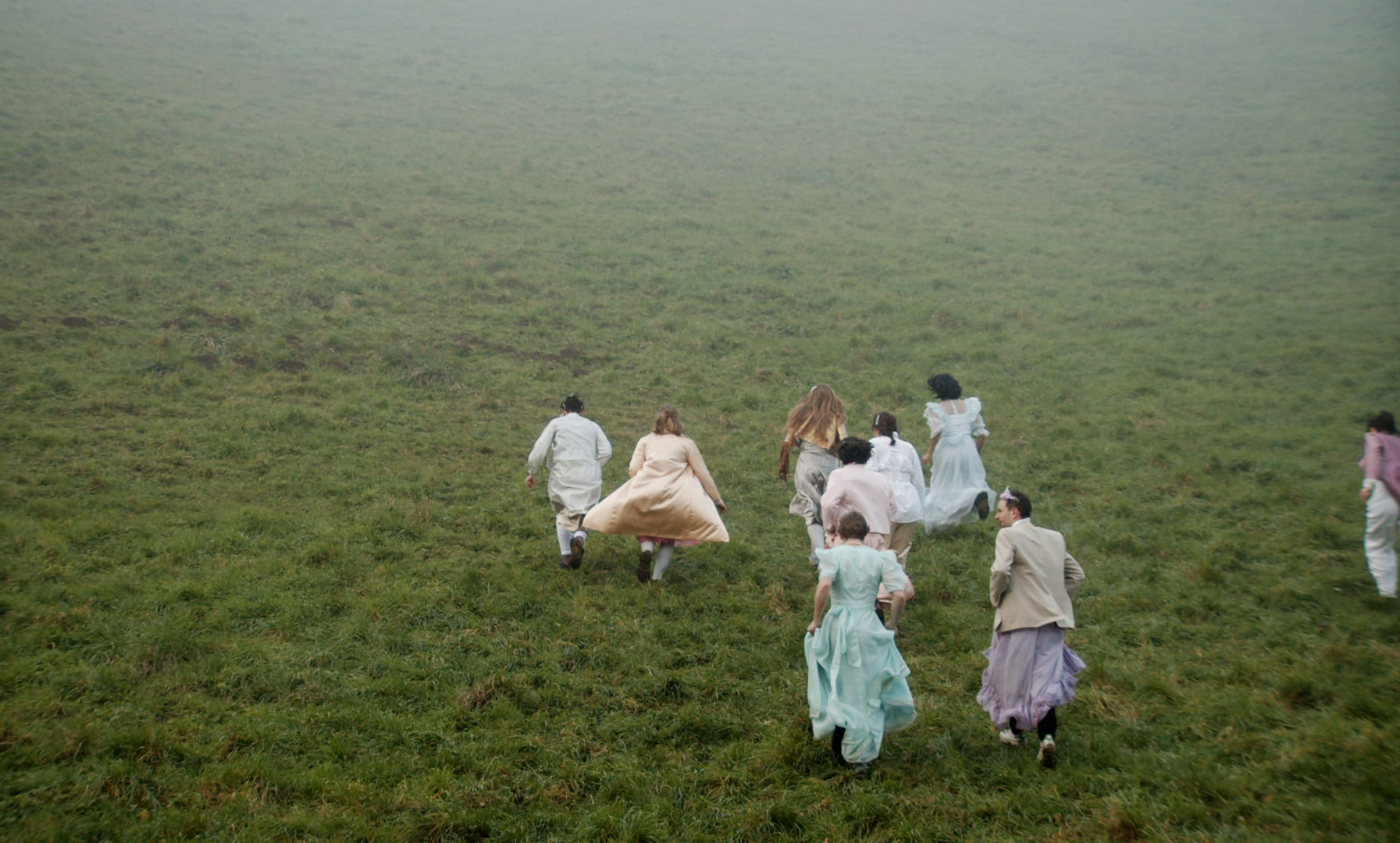 A crowd of people in white dresses running up a grassy hill in the fog.