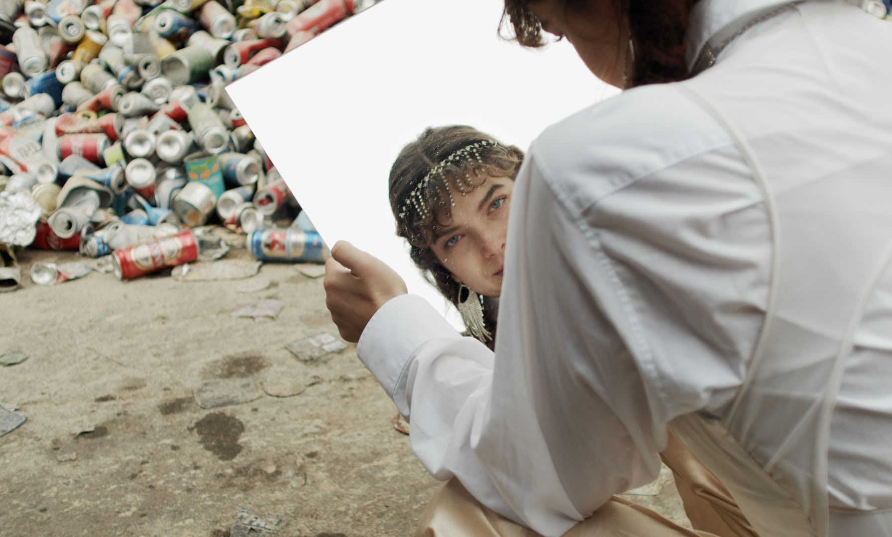 A young woman looking through a mirror in her hand into the camera.