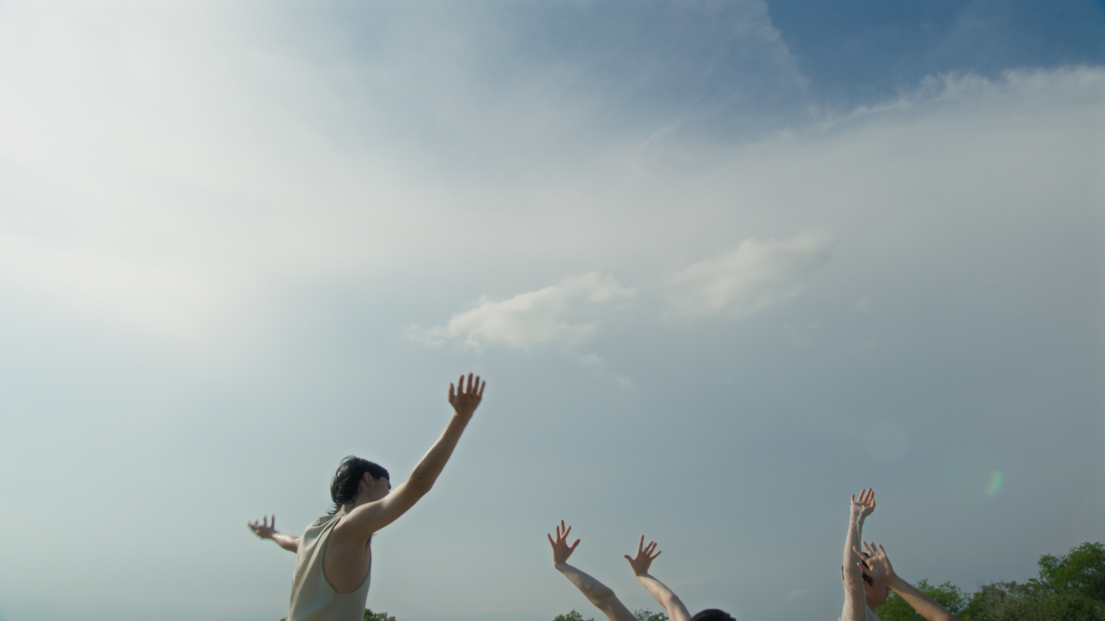 The arms of several young people reaching up into the sky.