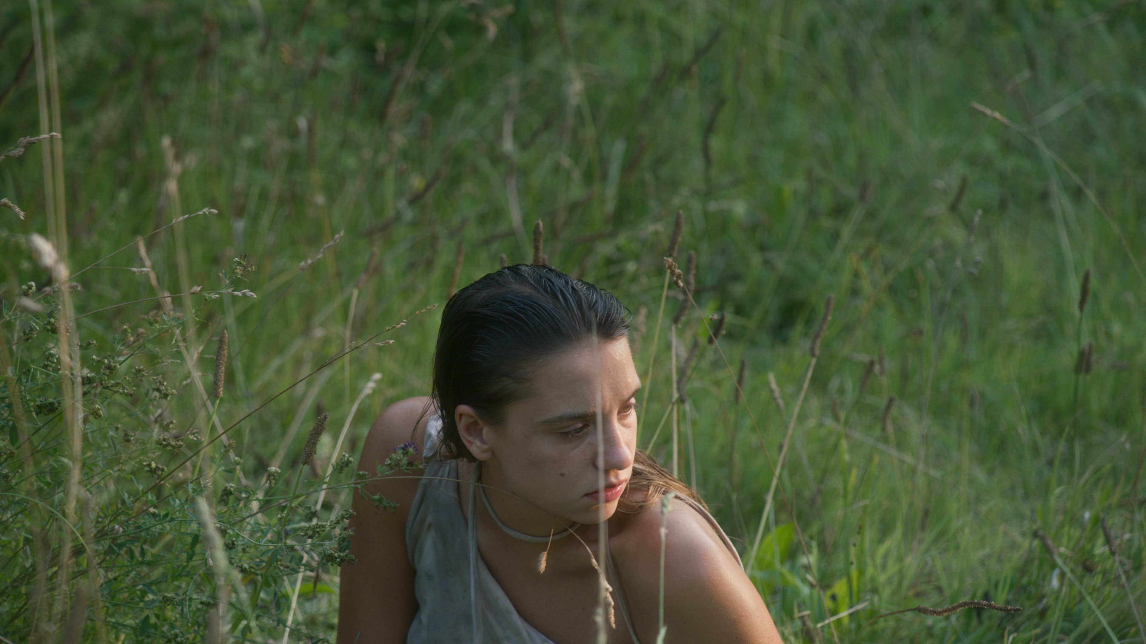 A young woman with wet hair is sitting in a field of tall grass. 