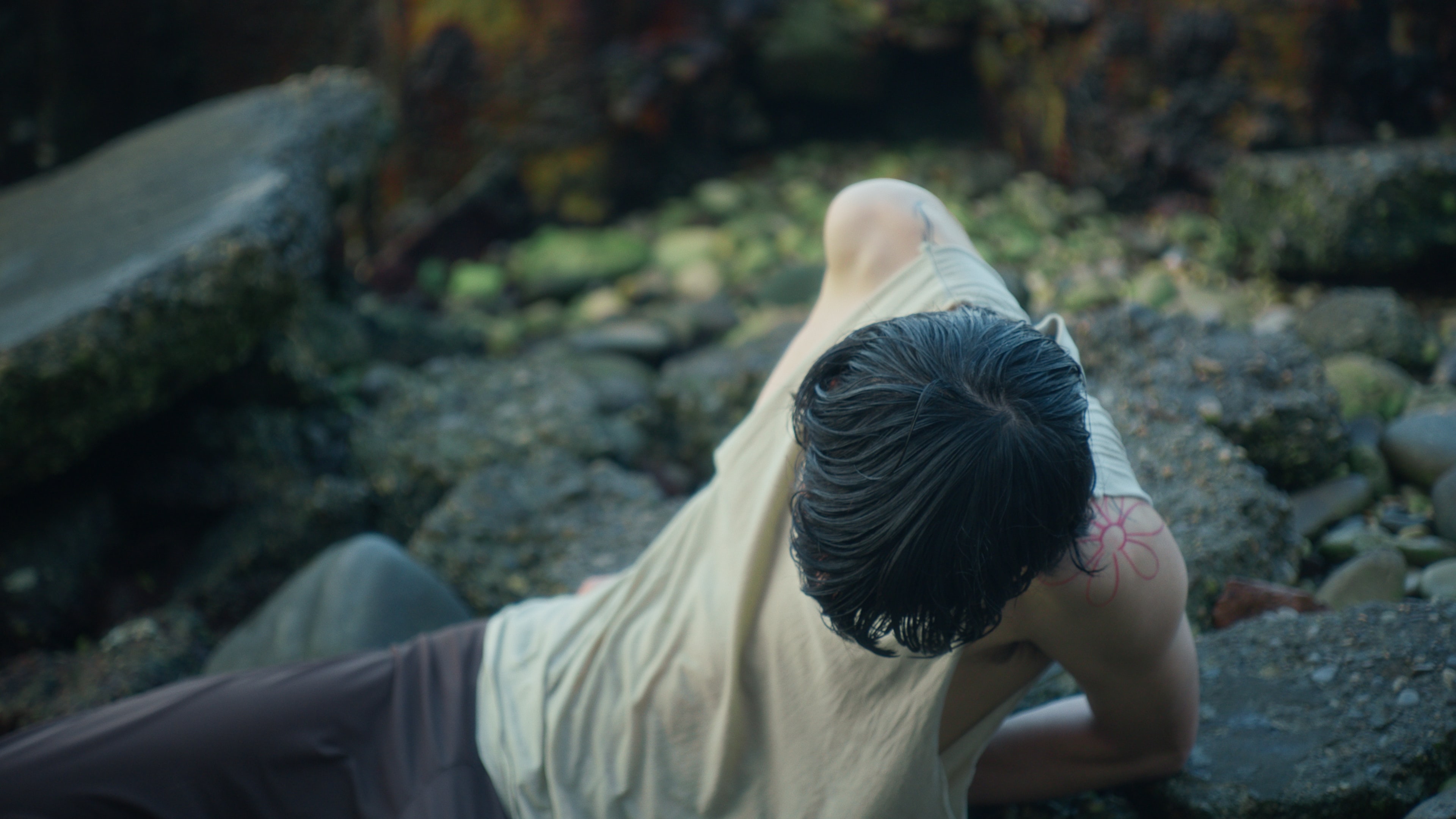 A young man wearing wet clothes laying on wet stones, covered in algae.