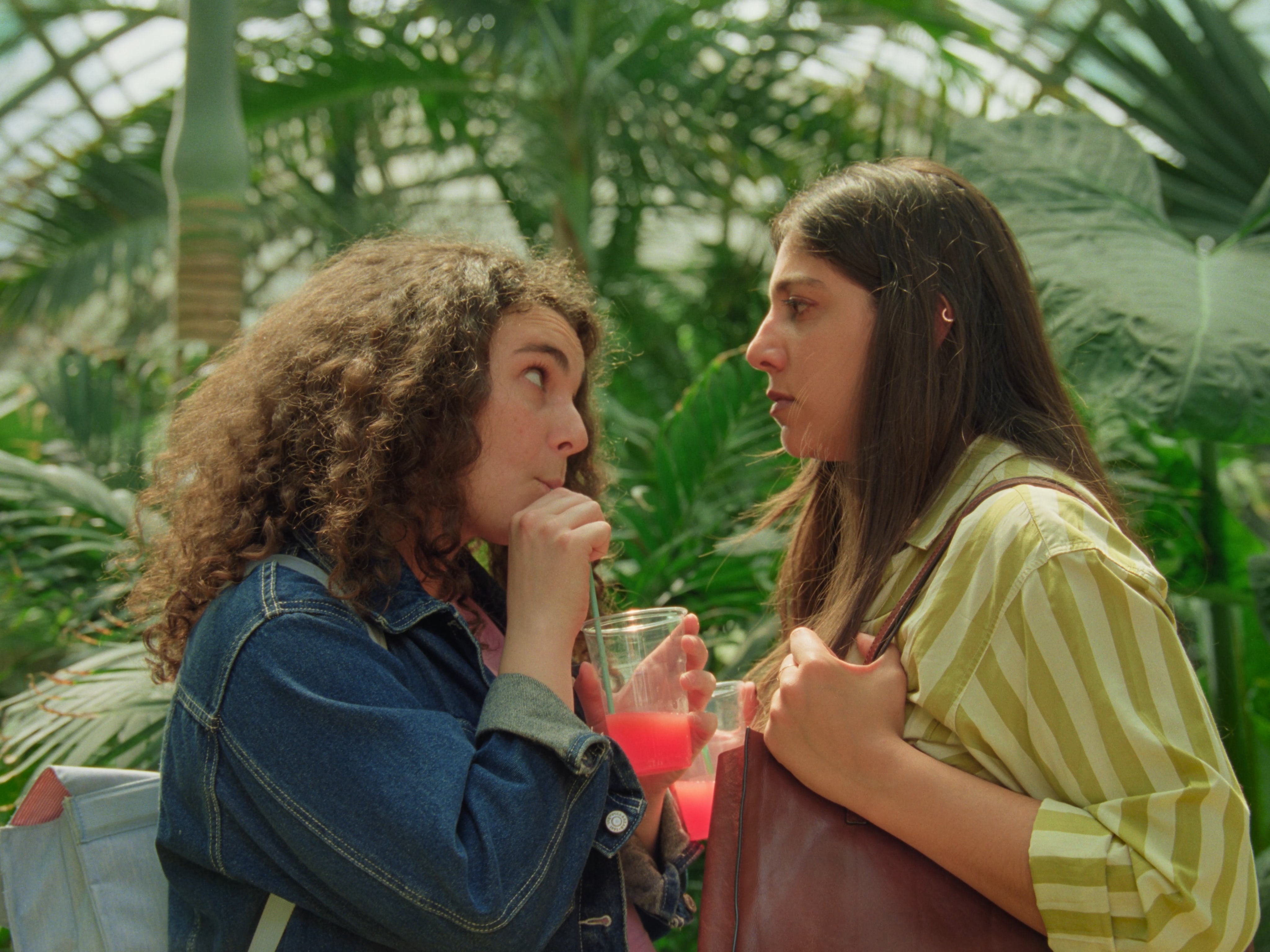 Two women facing each other, drinking from a plastic cup.