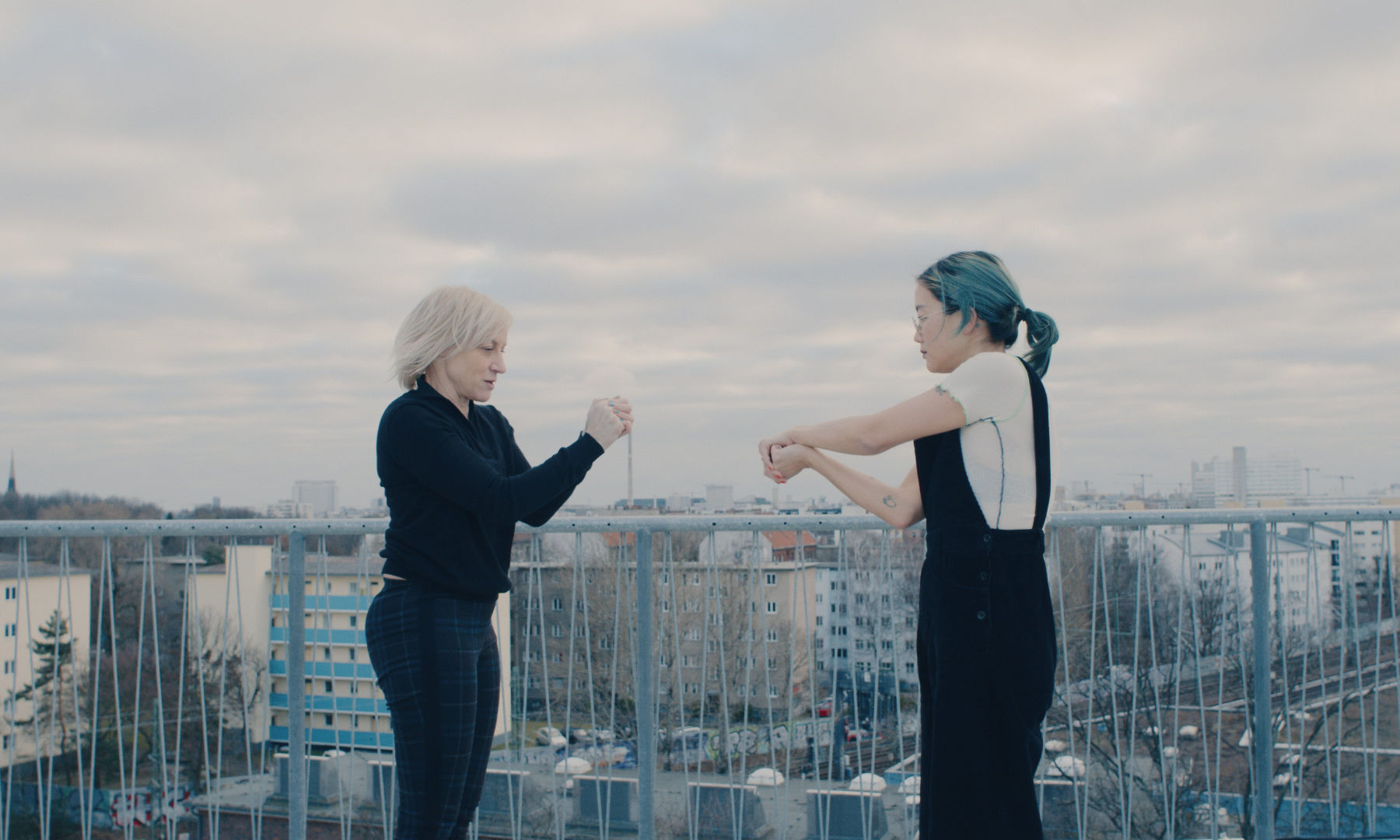 Christine Sun Kim and Meg Stuart dancing on a roof top, Berlin skyline in the background