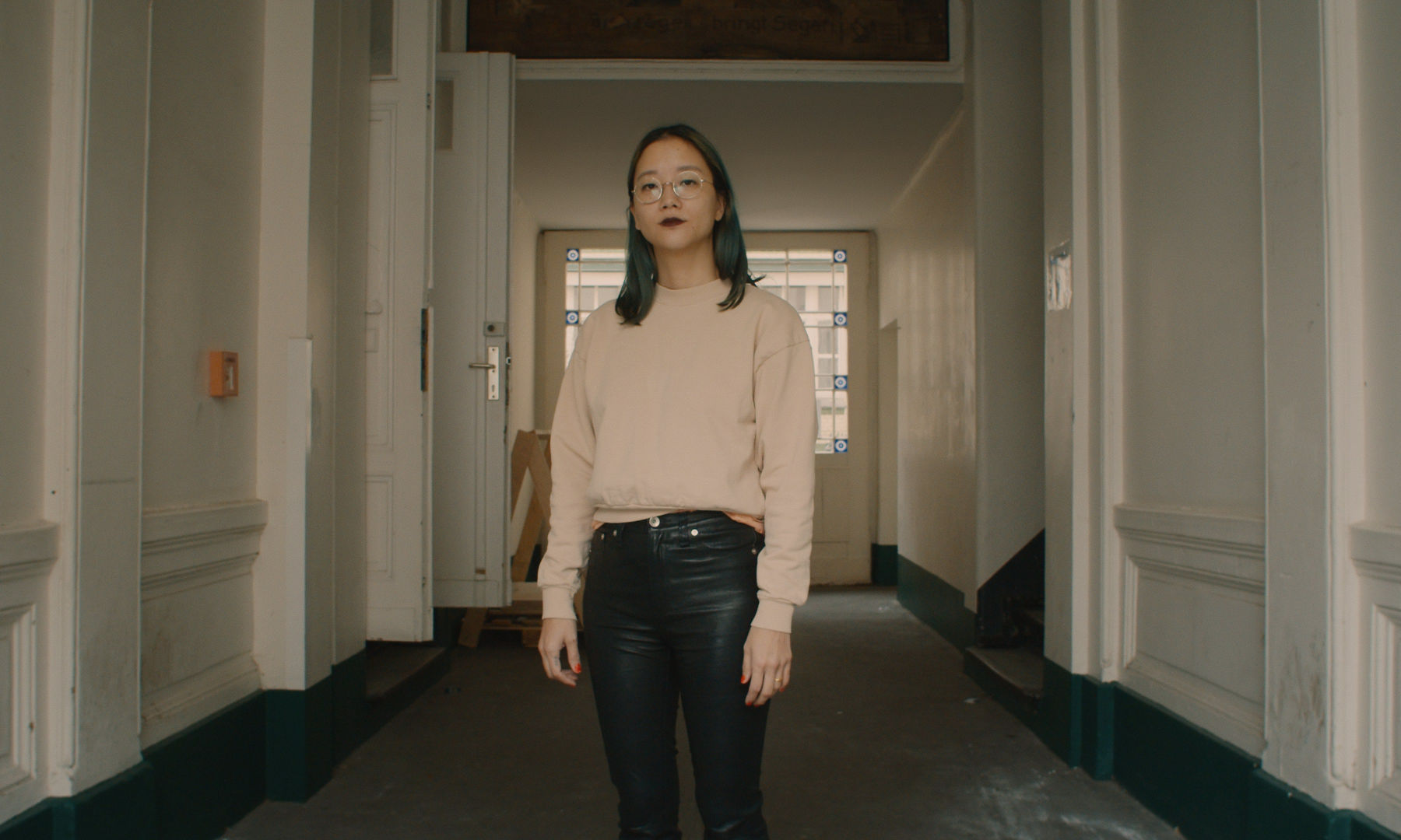 Christine Sun Kim standing in the hallway of an old building. 