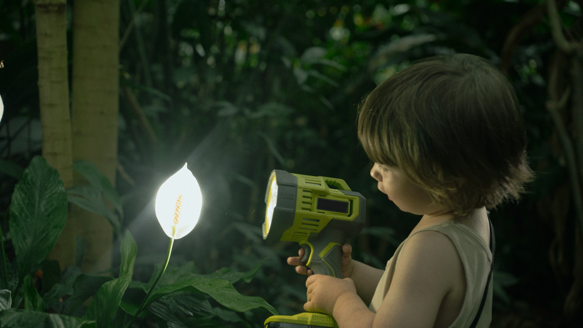 A young boy examining a flower with a very large flashlight