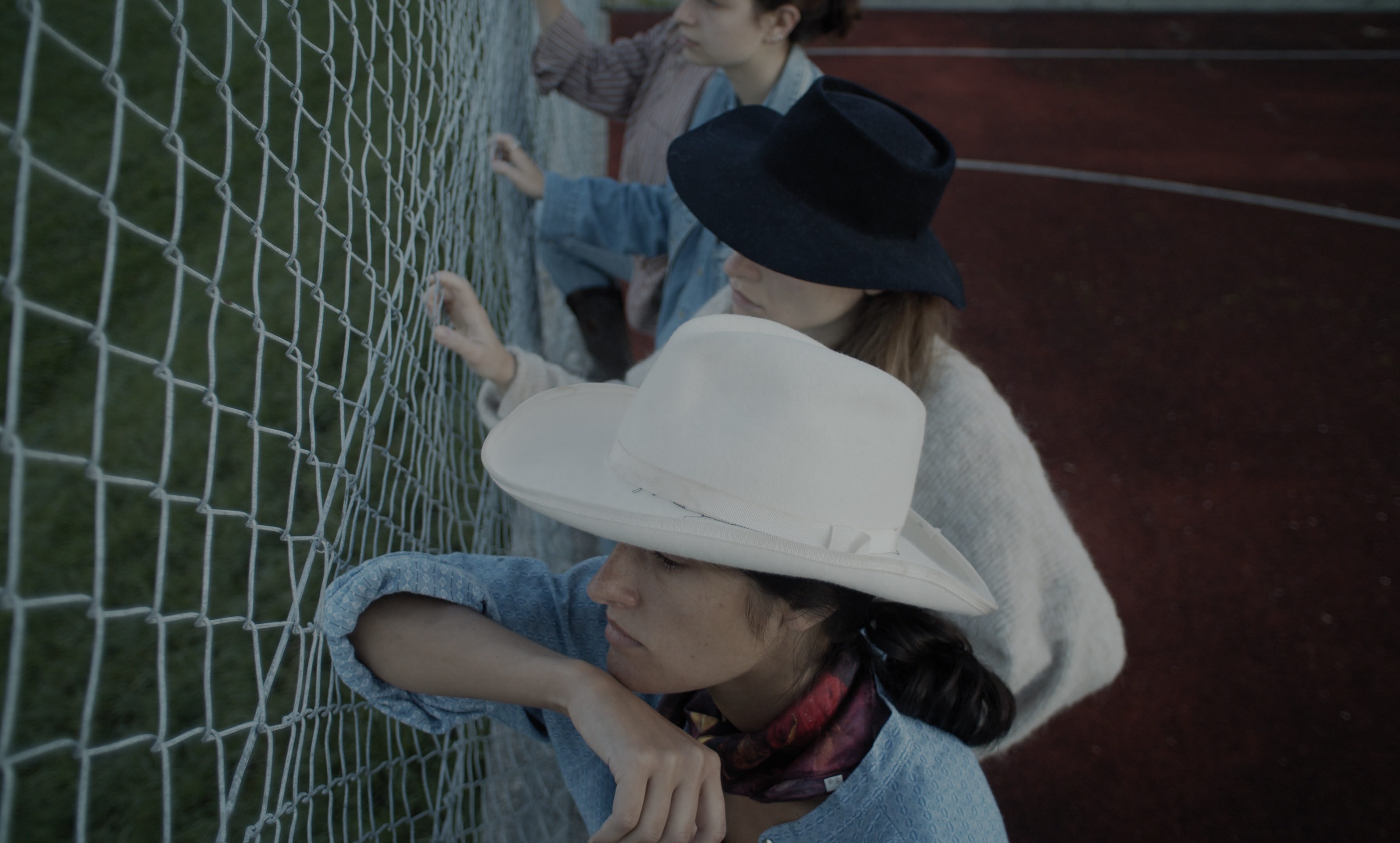Four women, seen from above, leaning against a chain link fence. They are wearing cowboy hats.