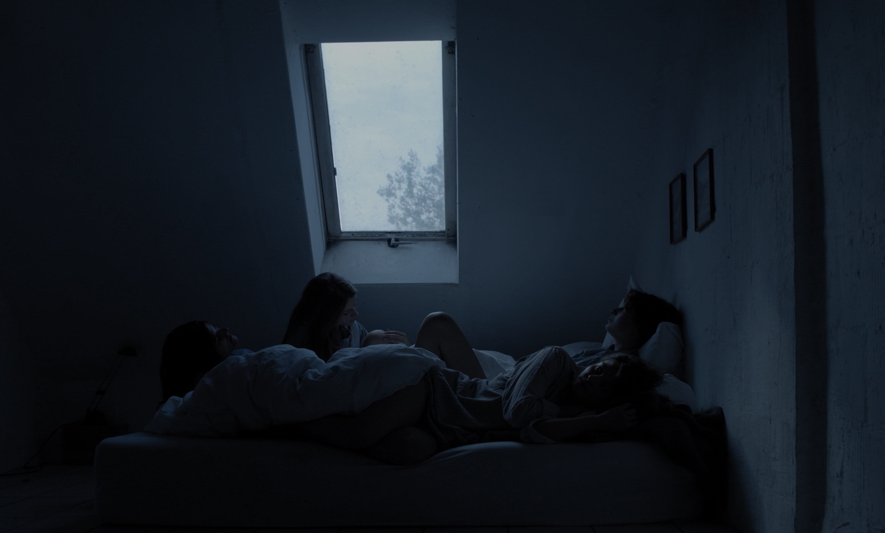 Four women lying in bed, waiting for something. Early morning light falls through the window. 