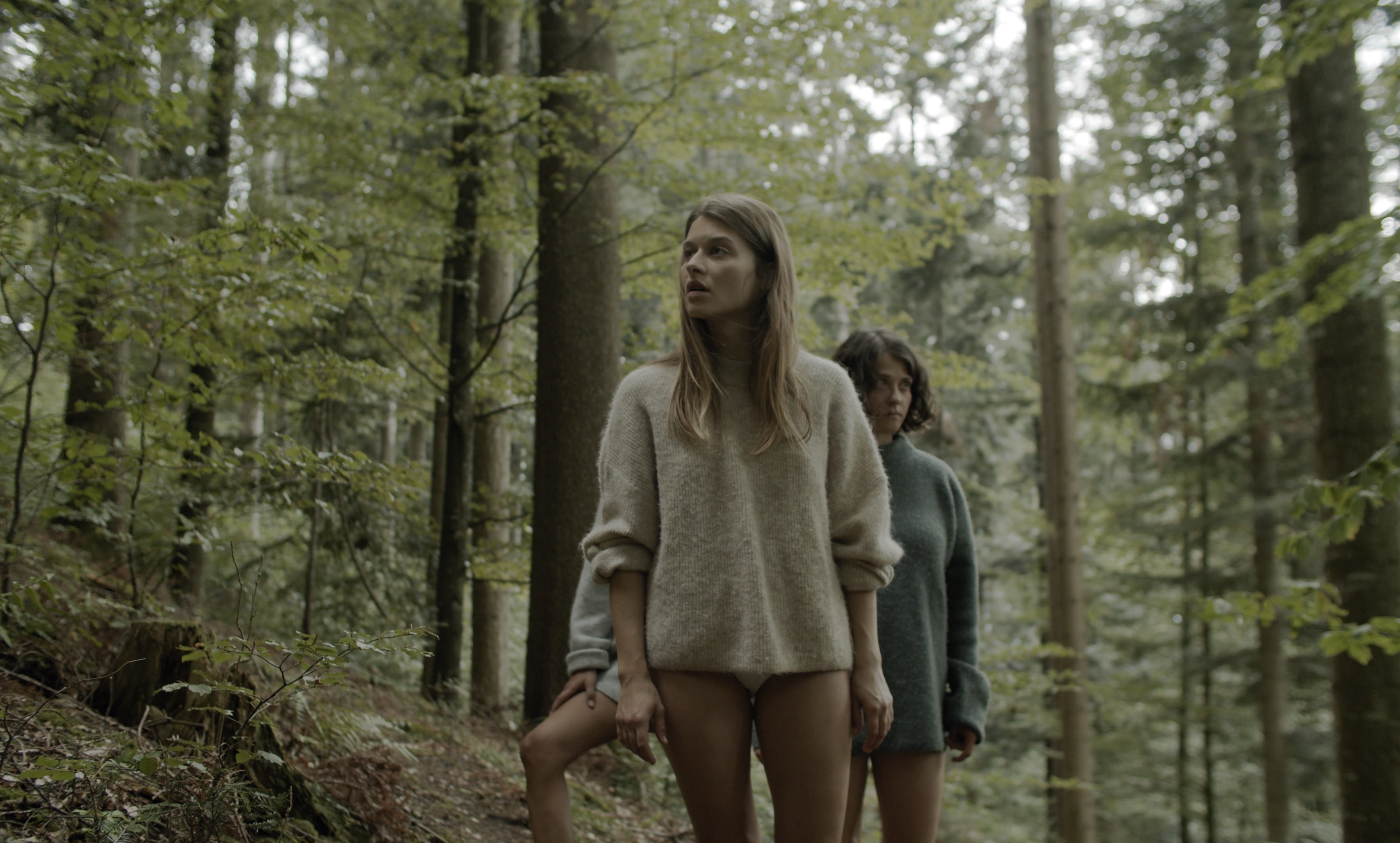 Three women with bare legs standing in a forest, looking around and searching. 